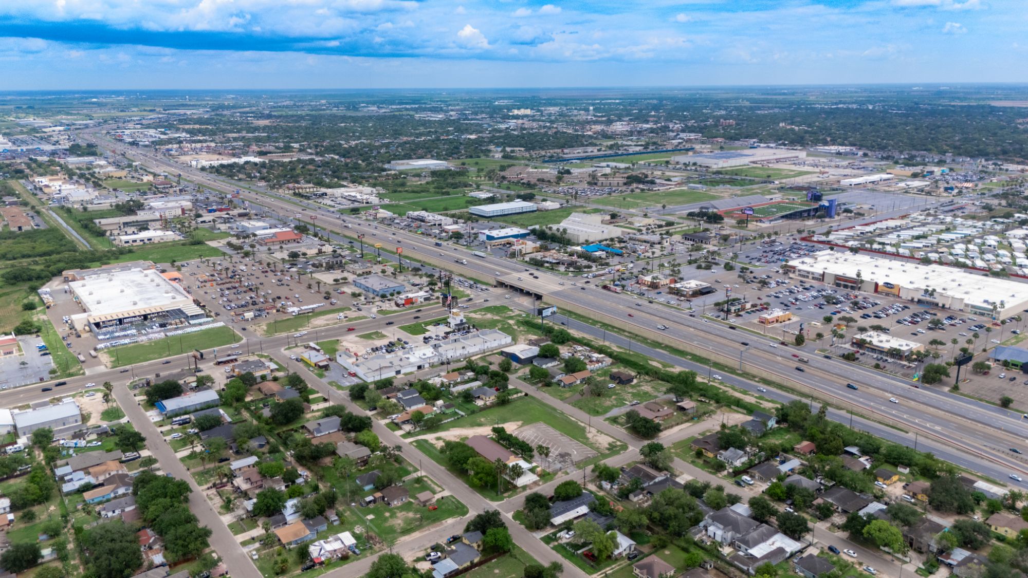 Aerial view of a South Texas retail corridor along a major expressway, with multi-tenant centers, big-box retail and the neighborhoods they serve